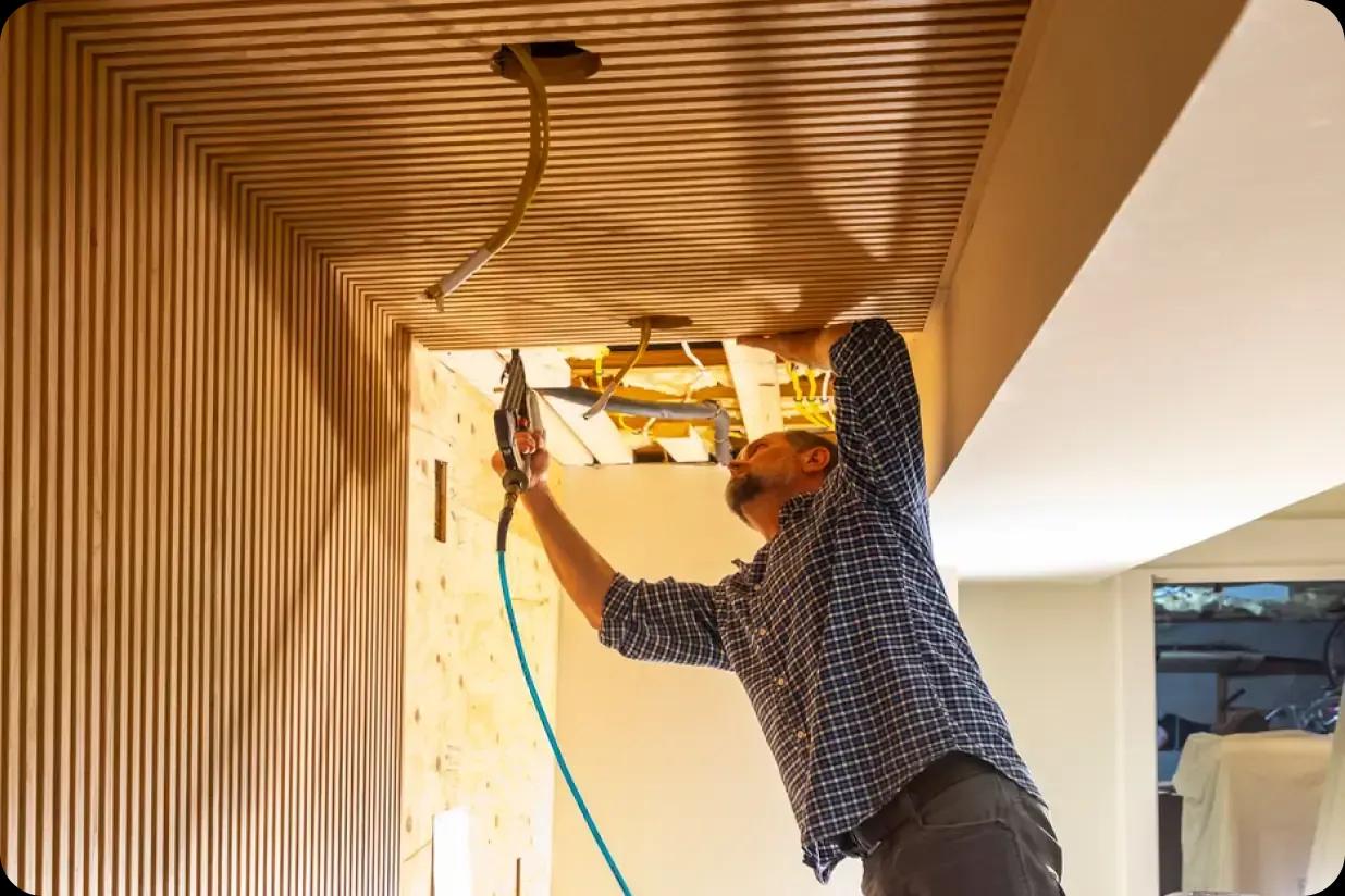 A man nailing decorative trim to the ceiling